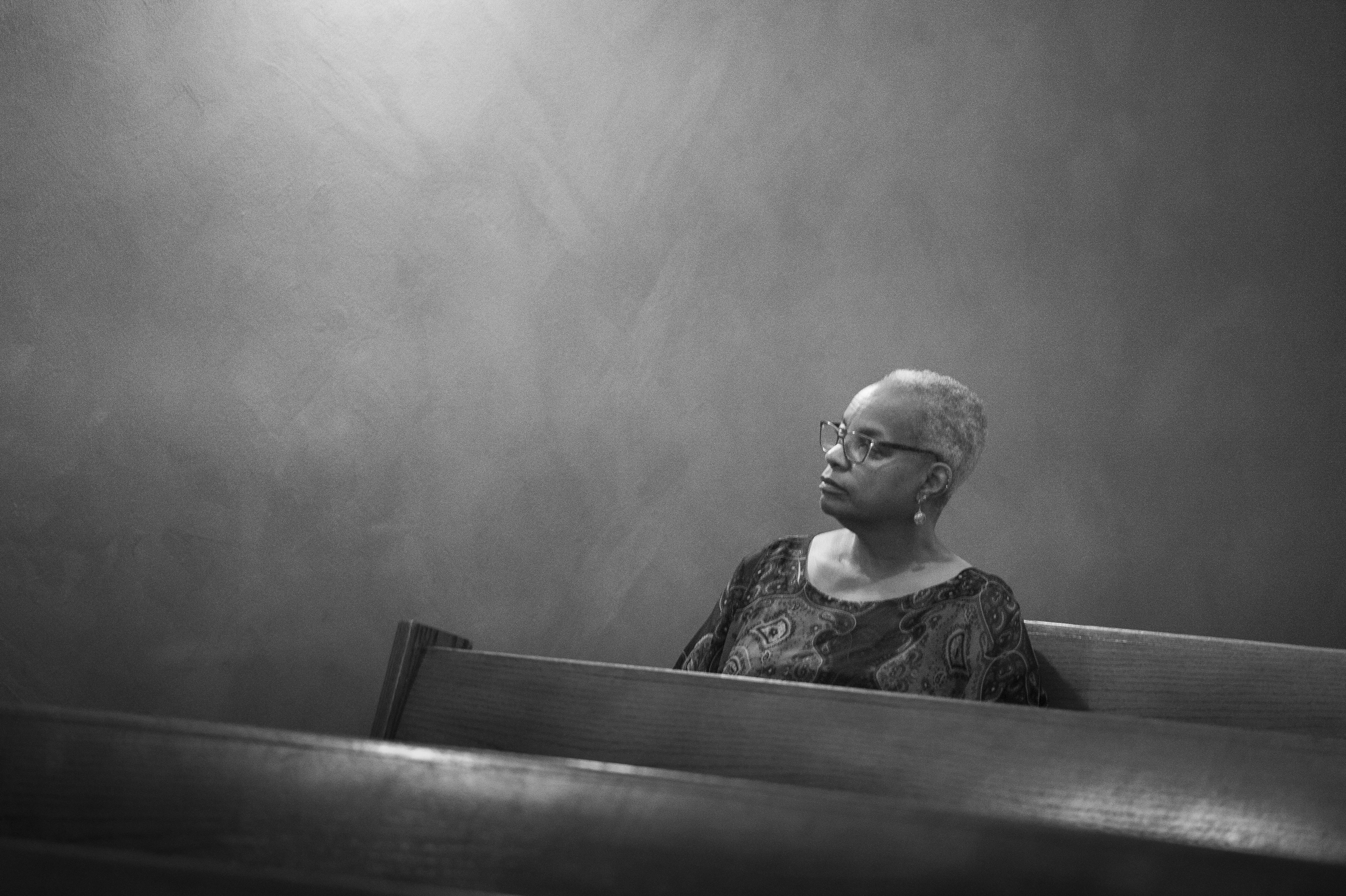 Black and white photo of woman alone in church pew by Hasna Muhammad