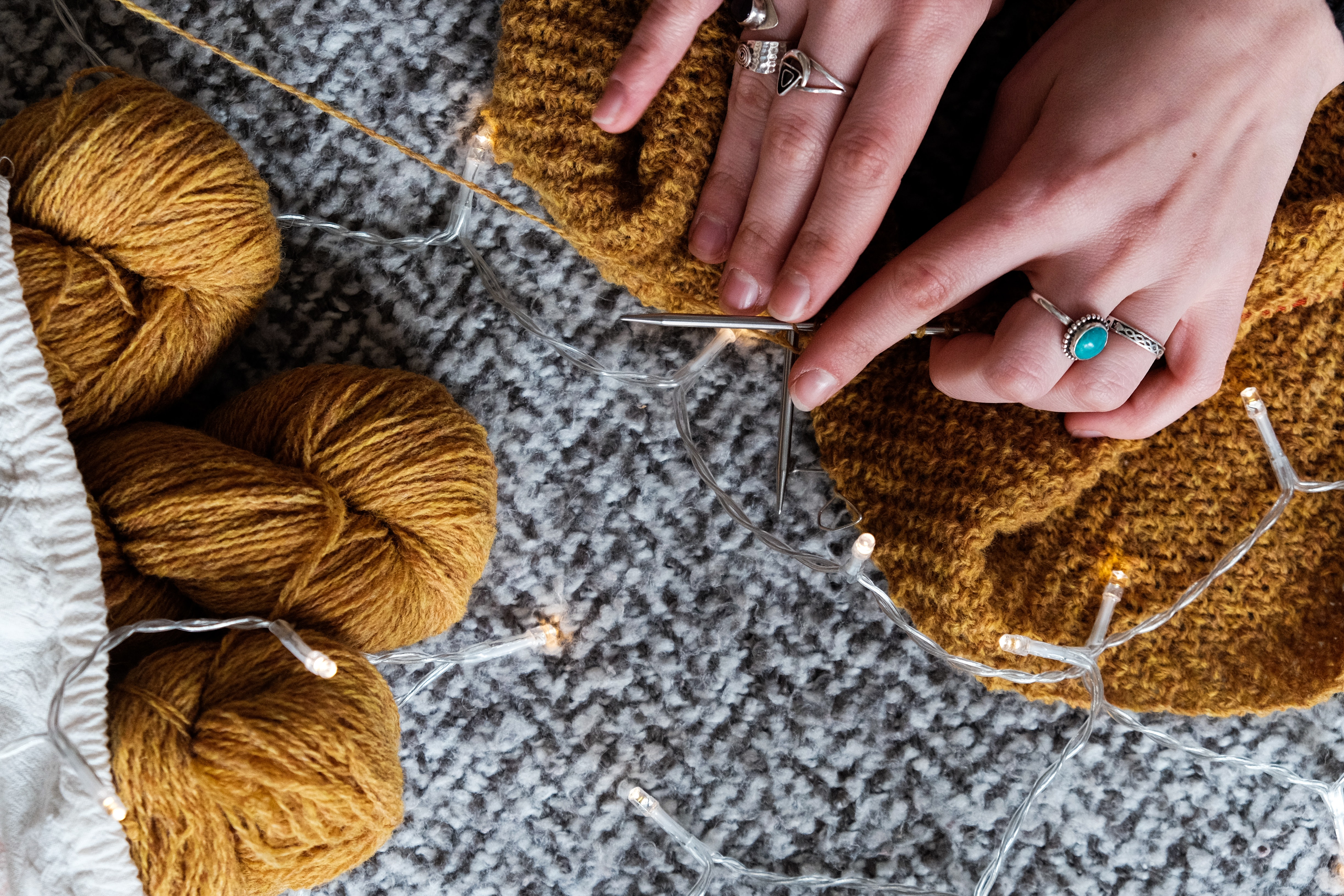 Hands with knitting needles, knitting mustard-yellow and gray yarn.