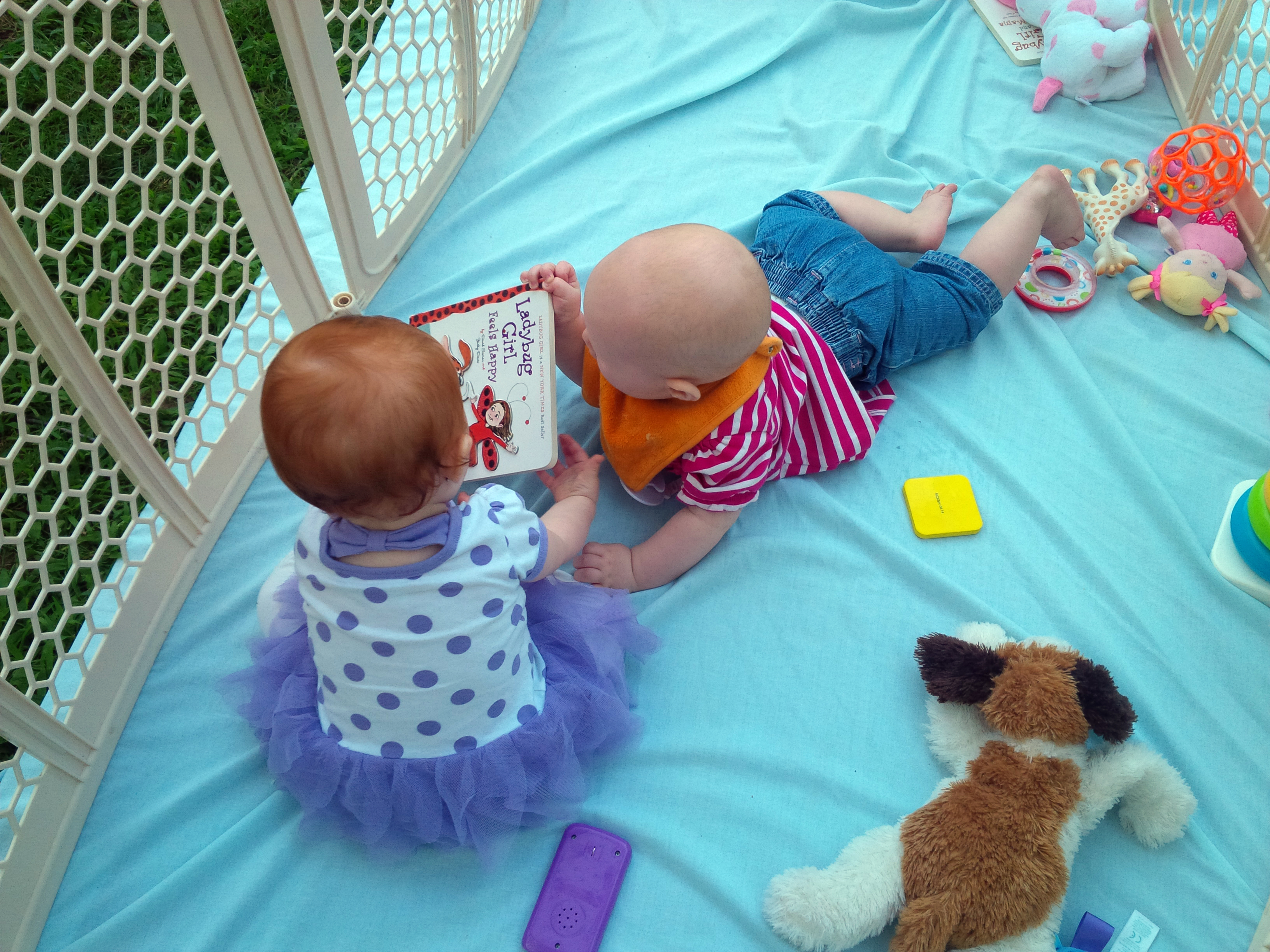 two babies looking at a book, surrounded by toys
