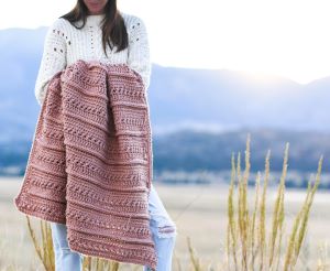 woman holds pink crochet blanket in a valley at sunset
