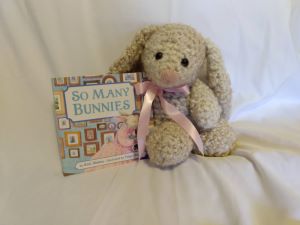 crochet bunny with pink ribbon sits with "So Many Bunnies" board book