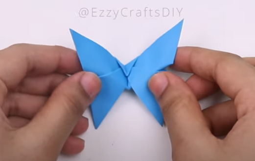 Image of a blue origami butterfly held by its wings by two hands.