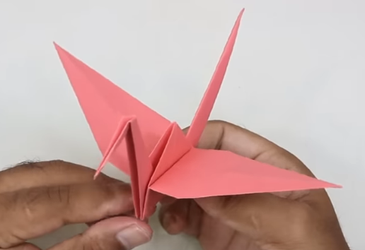 A pair of hands holds a red origami paper crane by its base.