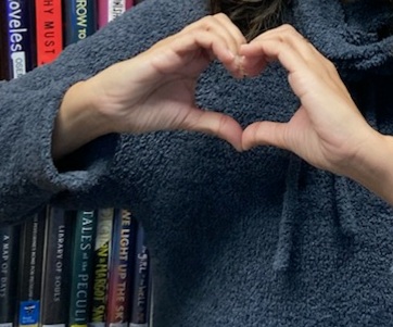 human hands making a heart in front of a bookshelf of books