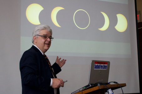 Photo of Joe Rao in front of a projection screen showing phases of the Sun and Moon