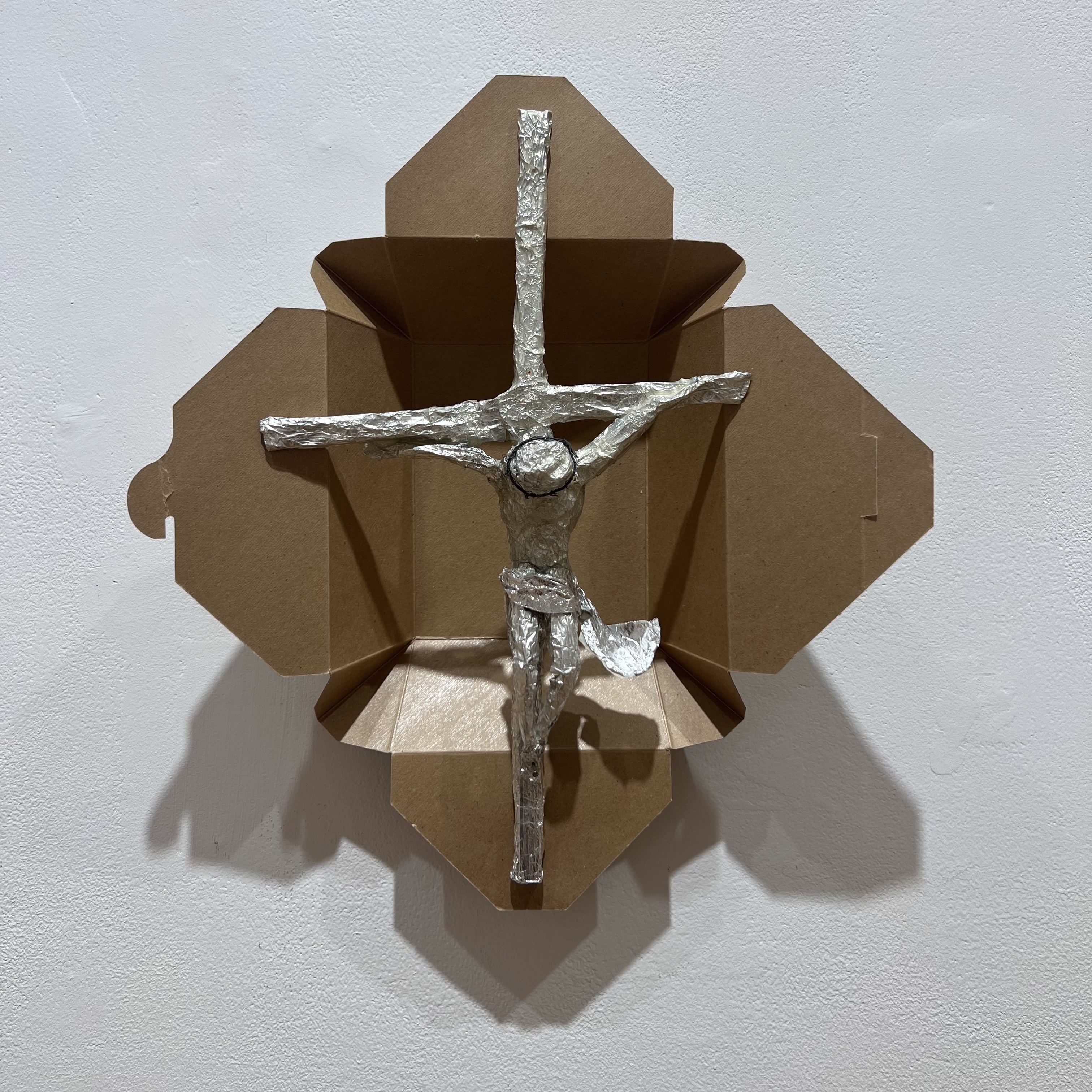 Aluminum crucifix sculpture on a cardboard takeout box