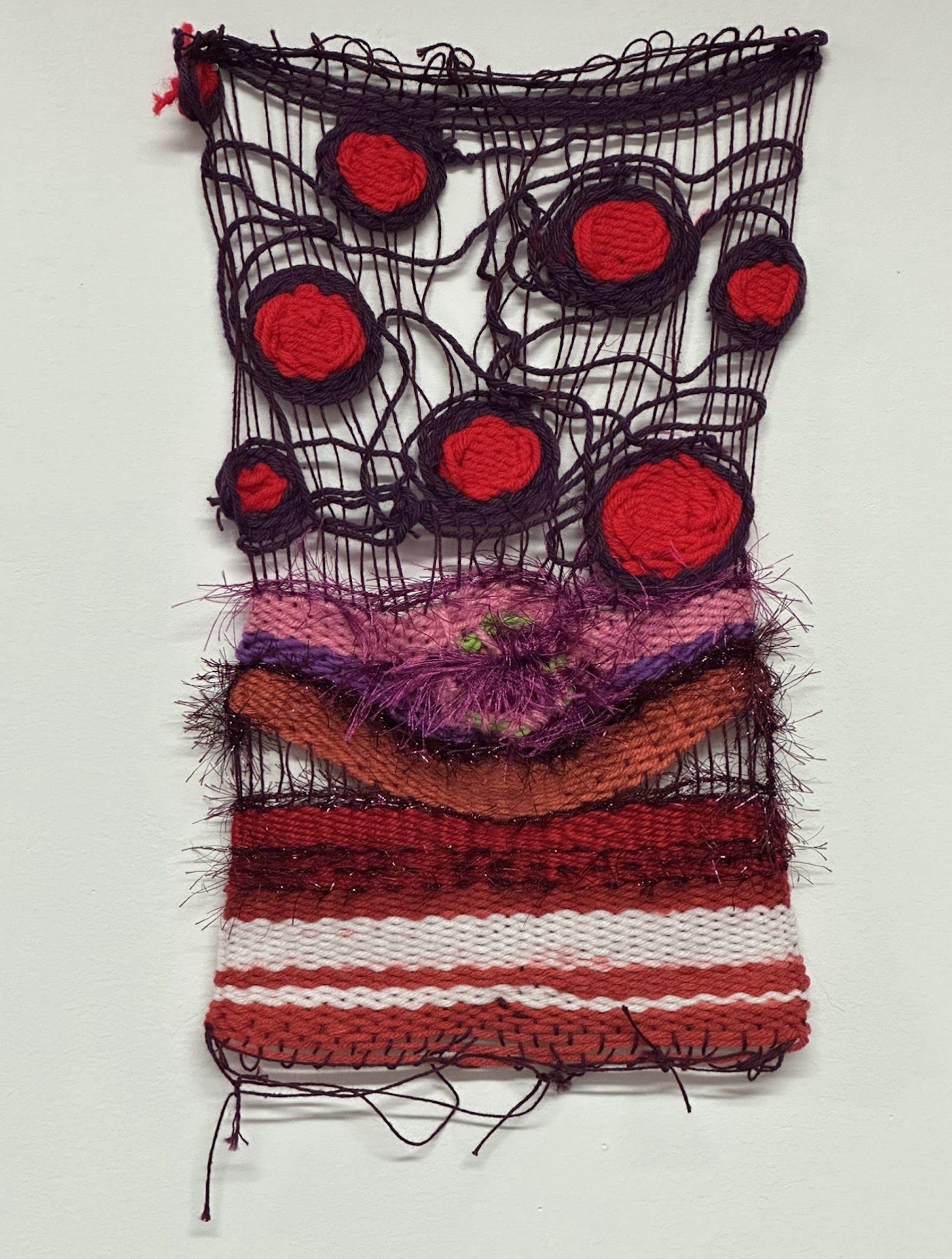 Red, pink and black textile weaving of red circles and horizontal lines