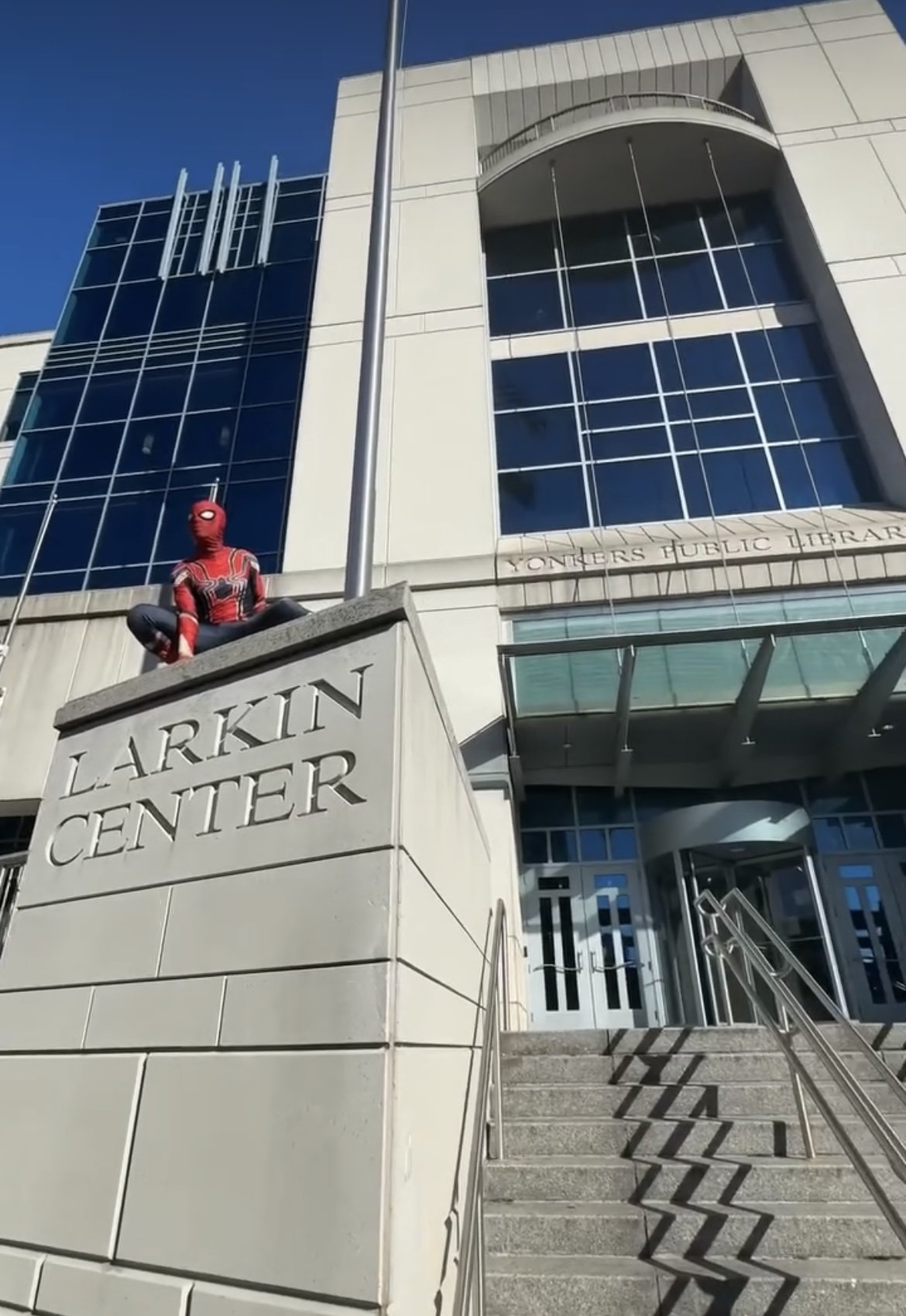 Person in Spiderman costume is perched near steps of Riverfront Library
