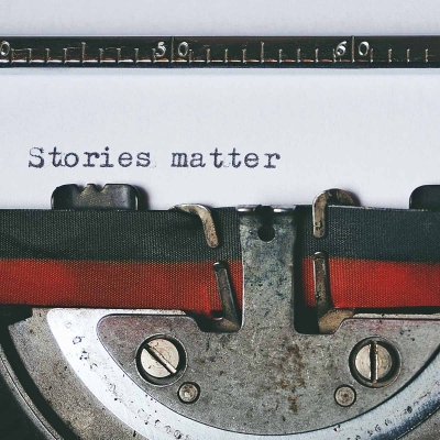 A typewriter, shown at a close-up. "Stories matter" is written on the page inside.