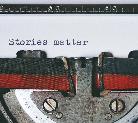 A typewriter, shown at a close-up. "Stories matter" is written on the page inside.