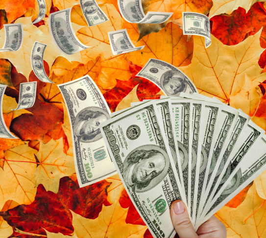Autumn Leaves in the background. In the foreground, loose money and a hand holding several $100 bills.