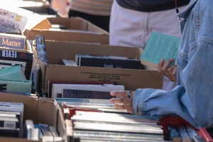Person looking through table of stacked books. 