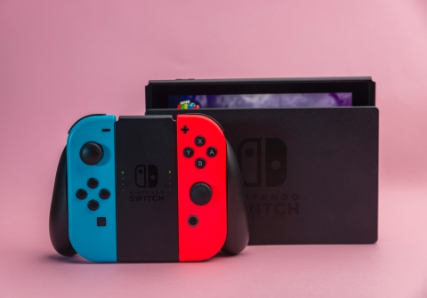 A black Nintendo Switch console sits on its dock. The red and blue controllers are in a the black handheld mode adapter in front of the dock.