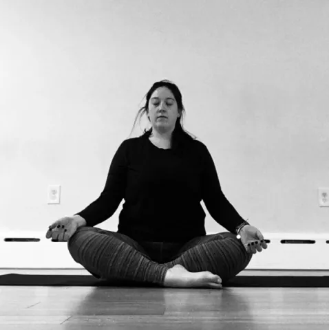yoga instructor Shannon Reilly in a cross legged position with arms rested on knees in angeli moudra
