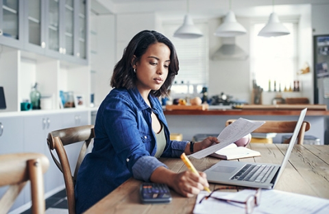 woman sitting at a computer with calculator, glasses pencil and a pad of paper