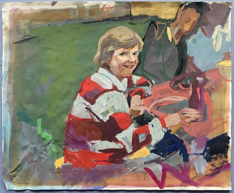 Woman sitting at a table smiling and looking over her shoulder to the audience. She is wearing a white and red striped shirt.