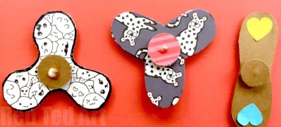 three fidget spinners of different shapes on a pink background