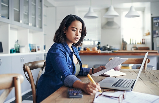 woman sitting at a computer with calculator, glasses pencil and a pad of paper